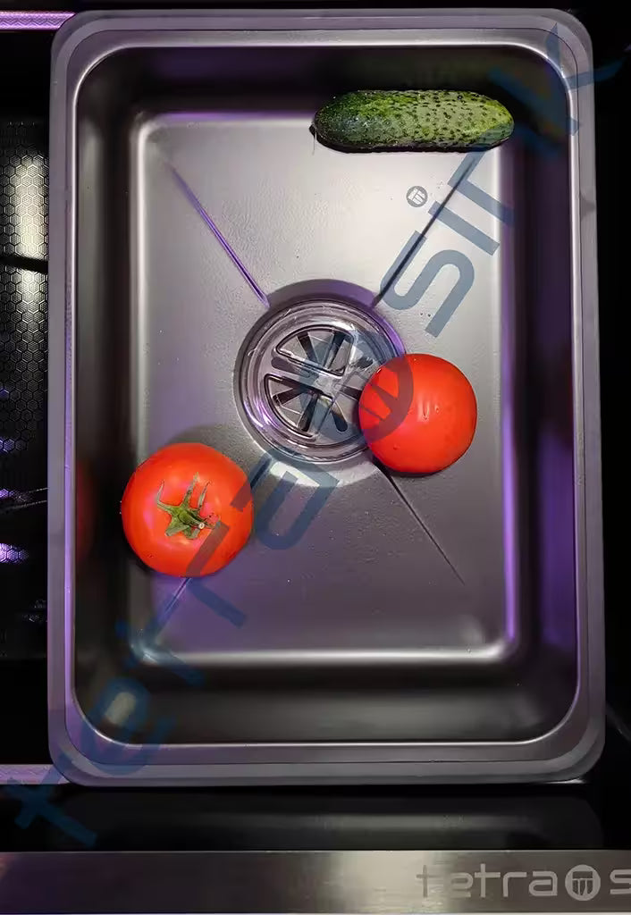 Stainless steel sink with tomatoes and a cucumber on a dark surface